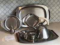 Lot displayed on counter including kettle, cream and sugar set, trays, and egg timer