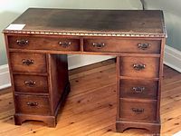 Front view of wooden campaign style double pedestal desk with decorative carved edge and seven drawers, showing metal pull handles.