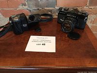 Two cameras on wooden surface: Nikon Coolpix 4500 digital camera and Pentax Asahi Spotmatic 35mm film SLR camera with lens attached.