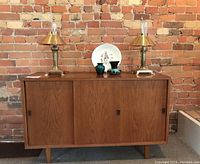 Front view of teak sideboard against brick wall with decor on top