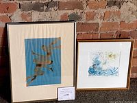 Both framed artworks leaning against a brick wall