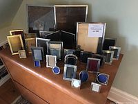 Overview photo showing 23 picture frames set on a wood surface with different sizes and styles including rectangular, oval, and circular shapes in brass and silver tones.