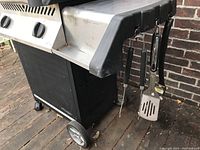 Right side shelf with hanging grill tools (spatula, tongs, grill brush) and wheels visible