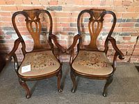 Two mahogany armchairs side by side against brick wall