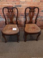 Pair of mahogany chairs with curved backs and needlepoint floral upholstered seats against brick wall background.