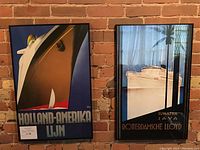 Two vintage cruise posters framed in black metal hung on a brick wall, showing Holland-Amerika Lijn and Rotterdamsche Lloyd Sumatra Java.