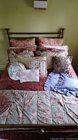 Full view of brass bed with two floral quilts layered and several decorative pillows arranged