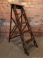 Front view of wooden folding ladder fully opened against brick wall