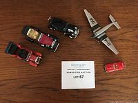Photo showing all five toys arranged on wooden surface: four cars and one airplane around lot number card.