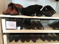 Shelf with brown leather ankle boots, black tall boots, and other shoes including Bruno Magli shoes