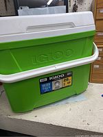 Front and top view of the green Igloo cooler with white handle, showing embossed brand and sticker label.