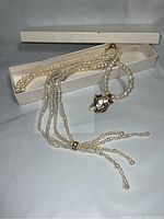 Full view of two pearl necklaces displayed on white box, showing extended strands and pendant details.