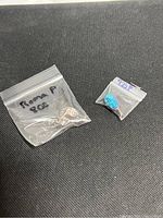 Two pendants in small ziplock bags labeled with 'Roma 800' and '925'. One has a blue opal stone, the other is a textured silver pendant.