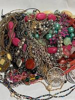 Photo showing a jumble of various necklaces including chains, beads, and pendants in mixed colors and materials.