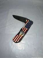Opened pocket folding knife showing blade with 'USA' inscription and handle with bald eagle and USA flag design.
