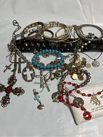 Overview of assorted gold, silver, leather, and beaded religious jewelry including cross pendants, bracelets, and necklaces arranged on a white background.