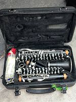 Open black hard case with sections holding disassembled black clarinet with silver keys, corked joints, cleaning brush, and cloth.