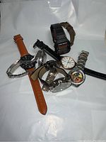 Seven men's watches laid out showing mix of metal bands, leather straps, and digital watch.