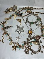 Overview of multiple ocean and beach themed gold and silver necklaces, pendants, and bracelets with charms shaped like starfish, dolphins, turtles, palm trees, and coral. Includes beaded and chain styles with pearl accents.