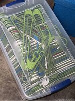 Top view showing a clear plastic tote filled with green and white plastic hangers stacked horizontally with a secure lid attached.