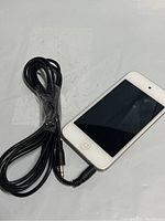 White Apple iPod laying flat showing front screen and home button along with black headphone cord