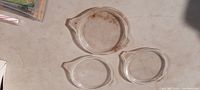 Three vintage Pyrex flat glass lids arranged on a table, showing full top view with visible dirt and stains.