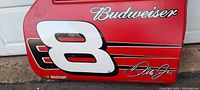 Close-up view of the red plastic car door sign with Budweiser logo, number 8, and Dale Jr. signature on white.