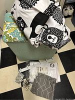 Photo showing multiple fabric shower curtains, a green fabric laundry hamper, white packaged shower curtain, and various curtain rings and hooks.