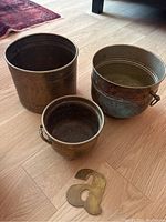 Three brass planters grouped on floor showing front and top views with patina and rust