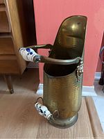 Front and side photo of a brass umbrella/cane holder with porcelain handles showing the item's shape, material, and condition.