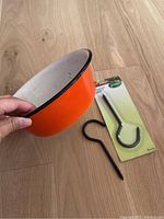 Orange enamel bowl showing exterior and one ceiling hook on floor next to it