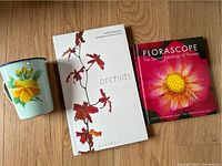 Photo of the vintage floral enamel mug alongside two flower-themed books titled 'Orchids' and 'Florascope'.