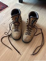 Full view of the pair of brown leather hiking boots showing overall worn condition and long brown laces untied.
