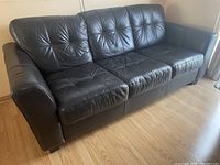Full view of black leather sofa showing three-seater design with armrests on each side and tufted cushions.