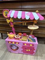 Front view of pink and purple mini cafe kitchen playset with canopy and kitchen accessories