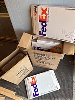 Photo showing open and stacked FedEx medium and small shipping boxes, mostly white with prominent FedEx logo.