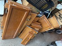 Set of 25 oak kitchen cabinet doors stacked on the ground showing varying sizes and metal hinges, need cleaning.