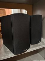 Pair of vintage black Paradigm wooden speakers with rounded front edges and black fabric grilles, positioned side-by-side.