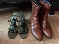 Pair of olive green strappy heels and brown leather ankle boots shown side by side on wooden floor.