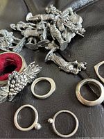 Close-up image showing pewter soldier figurines and silver rings on a black surface.
