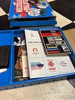 Blue plastic storage box containing vintage Canadian stamp album pages, reference booklets, and a black accessory holder