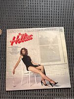 Front cover of The Hollies vinyl LP 'Long Cool Woman in a Black Dress' featuring woman in black dress sitting on a white chair.
