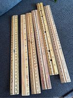 Group photo showing 12 vintage wooden rulers laid side by side on a flat surface. Various wood tones and slight wear visible.