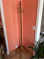 Full view of vintage wooden hall tree standing tall against a wall, showing entire height and base with legs spreading out for support.