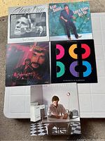 Photo showing five vinyl records laid out on a table. Albums include Glenn Frey, Ricky Skaggs, Lionel Richie, Toto, and Don Henley. Covers visible showing some wear.