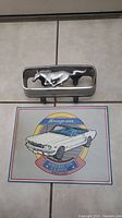 1966 Ford Mustang grille horse emblem and Snap-on metal sign laid on floor