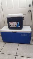 Photo showing the 28 quart Coleman cooler sitting on top of the 100 quart Coleman cooler, both with white lids, minor marks visible on surface.
