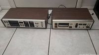 Two vintage 8-track players side by side on floor showing front panels and woodgrain cabinets