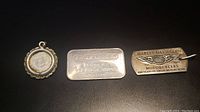 All three items laid flat: Engelhard silver bar, Guardian Angel silver coin pendant, and Harley Davidson sterling bar/pendant.