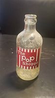 Front view of a single clear glass bottle with The Pop Shoppe label in red and white.